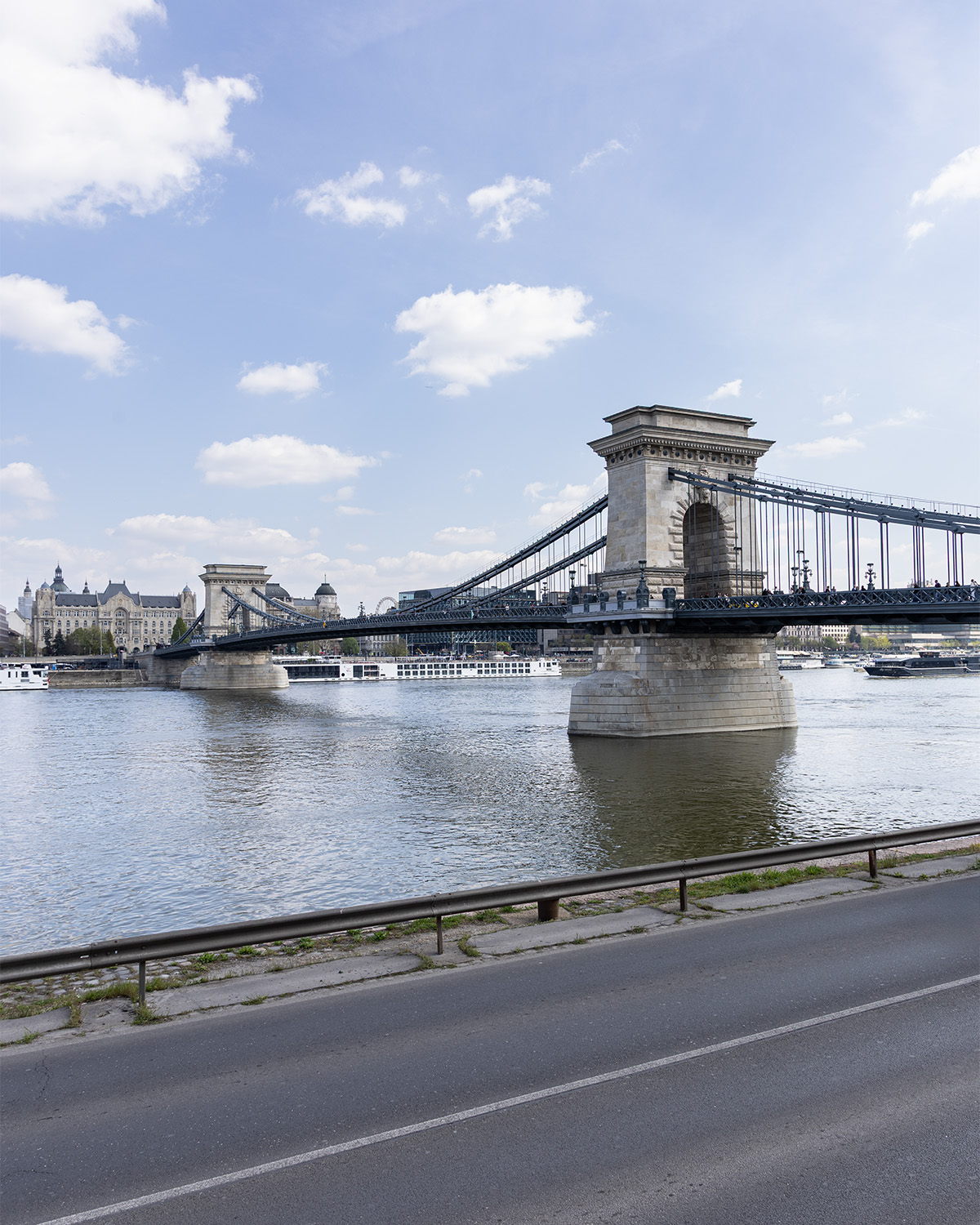 Chain Bridge in Budapest over the Danube River with city buildings in the background on a slightly cloudy day